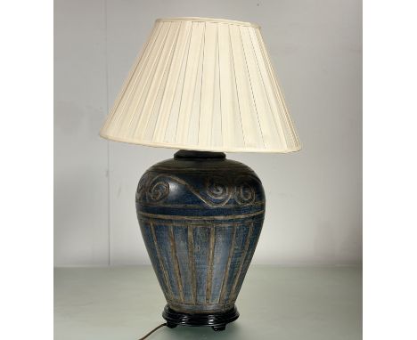 A large cast metal blue distressed style table lamp raised on a circular wooden base, with an cream coloured silk lampshade (