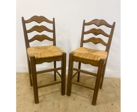 A pair of cherry kitchen stools, with shaped ladder backs above rush seats, standing on plain supports united by a stretcher,