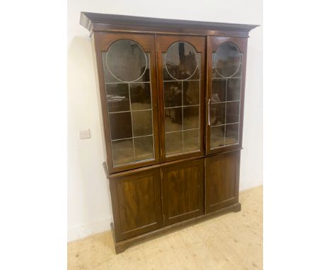 A large mahogany bookcase, with three leaded glass doors opening to reveal adjustable shelves, the base with three panelled c