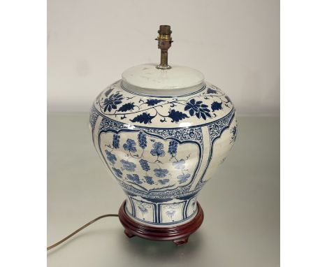 A large Chinese porcelain blue and white table lamp, with leaf and foliage decoartion, raised on a circular wooden base. 