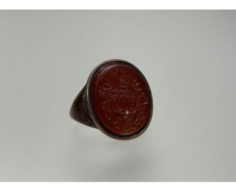 A carnelian intaglio signet ring, 19th century, the oval plaque engraved with a coat of arms, mounted in (unmarked) yellow me
