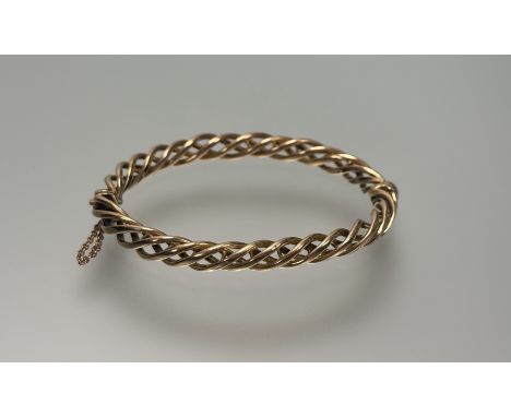 A yellow metal open-twist hinged bangle (unmarked) ,early 20th century, with safety chain. Internal width 6.5cm, 22 grams.