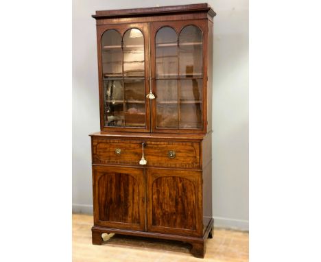A Regency mahogany two part secretaire bookcase with twin arched glazed panel doors enclosing three adjustable slide in shelv