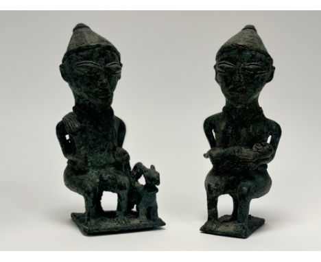 A pair of Yoruba (Nigeria) bronze figures of a seated couple: the man holding a fly whisk, a dog at his side, the woman holdi