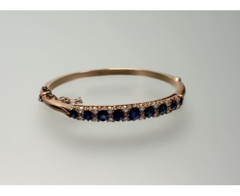 A sapphire and diamond bangle, c. 1900, set with nine graduated oval-cut sapphires spaced by pairs of round brilliant-cut dia