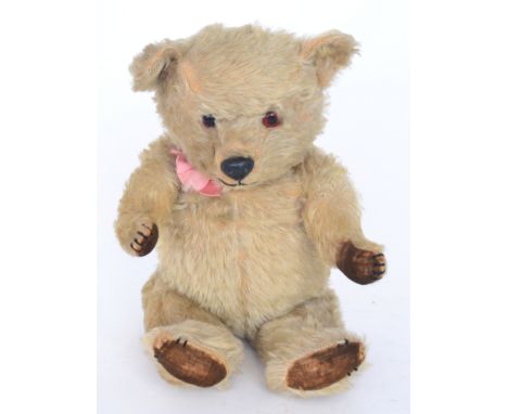 A 1950s Chiltern Hugmee blond plush teddy bear wearing a pink bow, brown felt pads and black plastic nose, length 41cm