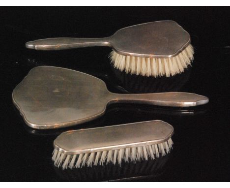 A hallmarked silver three piece dressing table set comprising of a hand mirror and two brushes, each with engine turned decor