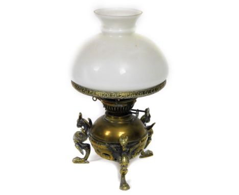 A 19thC brass oil lamp, with later opaque shade and cowl, the base applied with three winged griffin type figures, 35cm H.