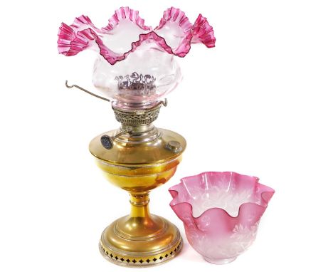 An early 20thC brass oil lamp, with cranberry and clear flared shade, fixed reservoir, inverted stem and circular foot, 45cm 