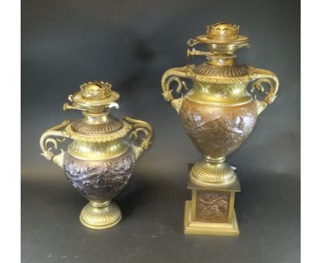 A pair of elaborate embossed brass and copper oil lamp bases with serpentine handles, the bodies with grape and vine, one wit