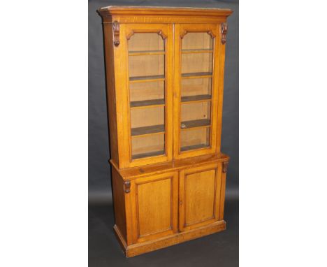 A Victorian oak bookcase cabinet, the moulded cornice above two glazed doors enclosing adjustable shelves on a base of two pl