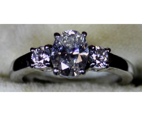 A platinum set three stone diamond ring, the central oval cut diamond approx 1.25 carats, flanked by two smaller stones, each