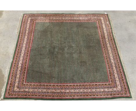 An Oriental carpet, the central green ground with all-over repeating motifs in salmon, black and cream, within multiple stepp