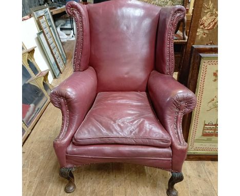 A George III style leather wingback armchair, on carved cabriole legs to pad feet