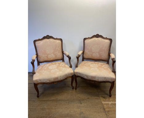 A pair of late 19th/early 20th century walnut framed armchairs, with a carved top rail, padded back, seat and arms, on cabrio