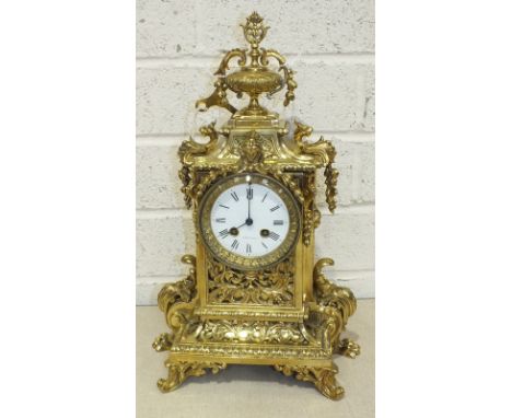 An early-20th century French polished brass mantel clock, the elaborate case with urn finial, circular white enamel dial and 