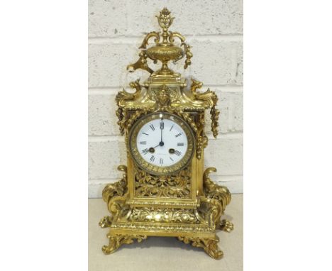 An early-20th century French polished brass mantel clock, the elaborate case with urn finial, circular white enamel dial and 