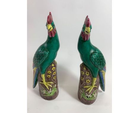 A pair of Chinese ceramic models of phoenixes, decorated in green, blue and yellow, each standing on a rock, 30cm high 