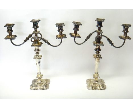 A pair of plated three light table candelabra, each with fluted scrolling arms and raised on a shaped square base, decorated 