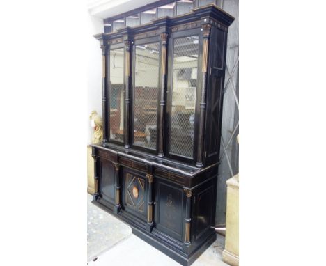 T. Oliver, Torquay; a Victorian Aesthetic Movement parcel gilt ebonised bookcase cupboard, with three glazed and grilled door