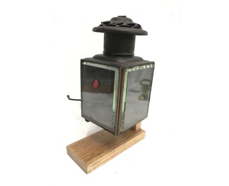 Oil lantern with two beveled glass sides and small red lens, four ball feet, contains burner. Height 22cm. Mounted on display