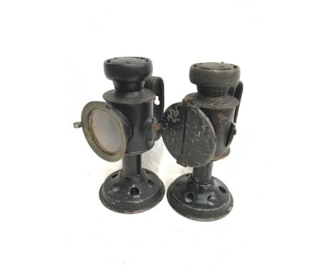 A pair of lanterns with clear glass lens (diameter 6cm), circular base, and bracket to rear. One with blackout cover, possibl