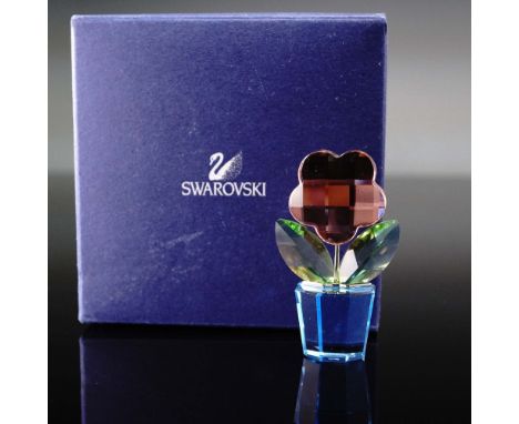 This Swarovski crystal flower figurine features a stylized pink crystal blossom with a faceted surface, vibrant green leaves,