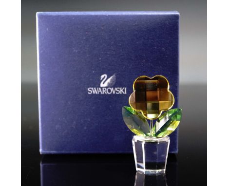 This Swarovski crystal flower figurine features a stylized yellow crystal blossom with a faceted surface, vibrant green leave