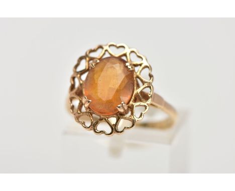 A YELLOW METAL CITRINE RING, designed with a claw set oval cut citrine, within an openwork heart shaped surround, stamped '9c