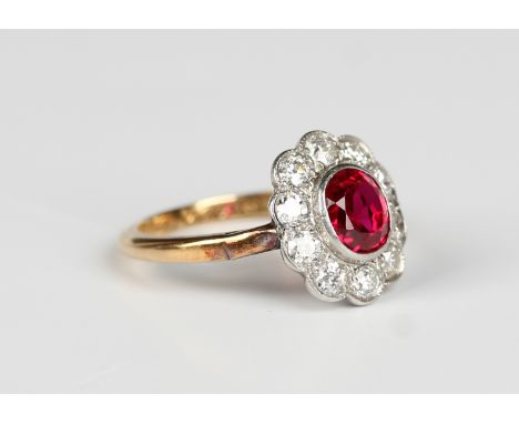 A gold, platinum, ruby and diamond oval cluster ring, collet set with the oval cut ruby within a surround of ten circular cut