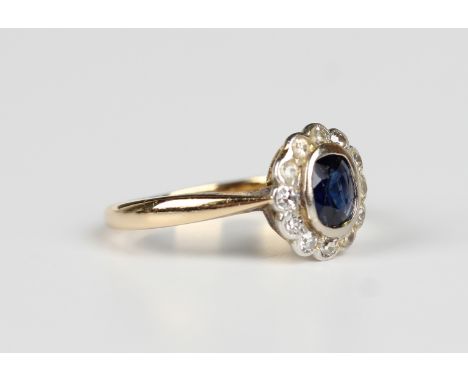 A gold, platinum, sapphire and diamond oval cluster ring, collet set with a cushion cut sapphire within a surround of circula