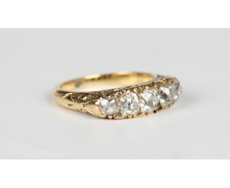 A gold and diamond five stone ring, circa 1900, mounted with a row of graduated cushion cut diamonds, the mount decorated wit