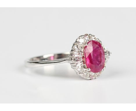 A white gold, treated ruby and diamond cluster ring, claw set with the oval cut treated ruby within a surround of circular, b