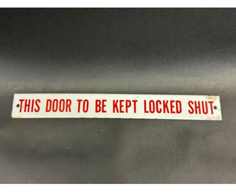 A small enamel sign bearing the words 'This door to be kept locked shut', 11 1/2 x 1 1/2".