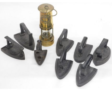 A quantity of flat irons, various makers and shapes, and a brass miner's lamp. 