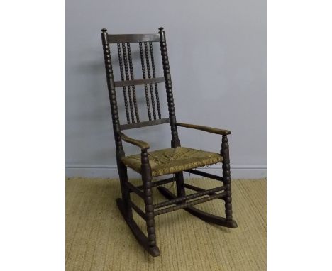 A brown stained ash and beech rocking chair in the manner of Ernest Gimson for Robert Weir Schulz with bobbin turned uprights