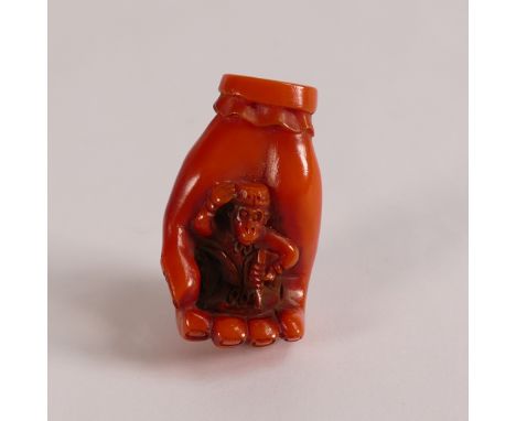 Japanese Coral Netsuke, in the form of dressed monkey in a large hand. Signed to base with two loop holes. Height: 4cm