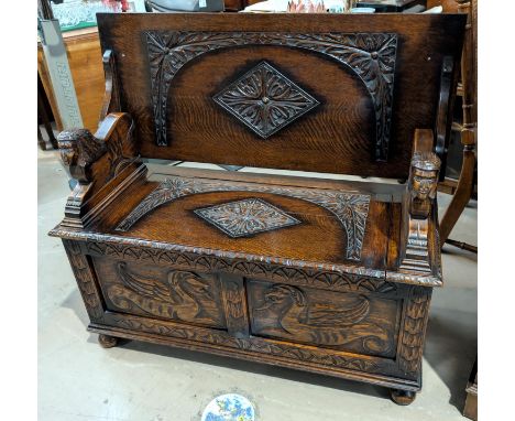 A carved oak monks bench with hinged storage and sphynx supports.