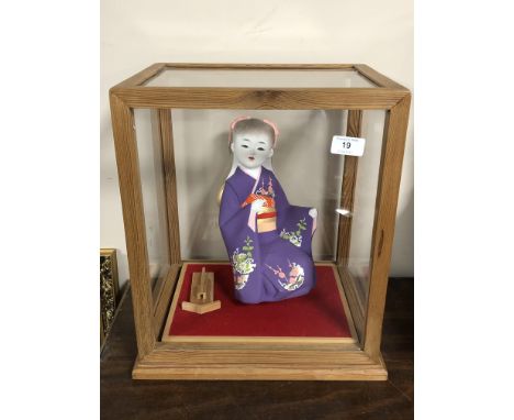 A contemporary matte-glazed Japanese doll/ornament, modelled as a young girl wearing a purple kimono, in a perspex and wooden