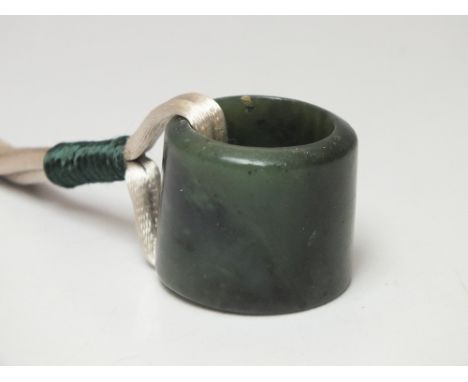 A CHINESE SPINACH JADE ARCHERS RING / THUMB GUARD, of plain form, H 2.7 cm, overall Dia. 3.1 cm, suspended from a silk cord