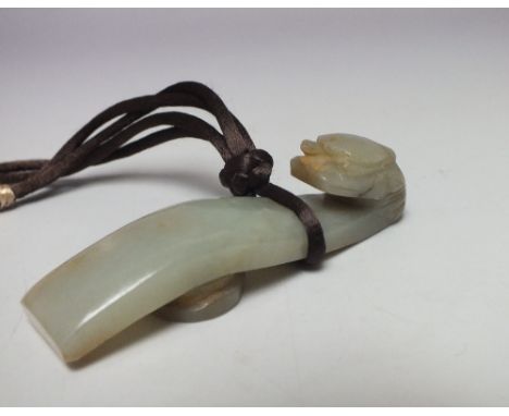 A LARGE CELADON JADE BELT HOOK, of plain form with carved mythical dragon to one end, having russet veining to reverse, suspe
