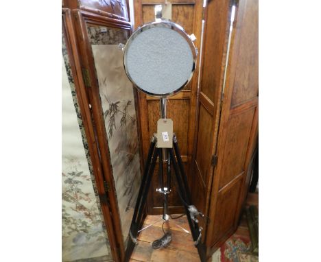 A chrome studio lamp raised on a tripod base. 