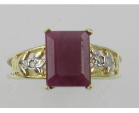 A yellow metal and ruby ring, the emerald cut ruby flanked by openwork shoulders with diamond accents, the shank stamped 9K. 