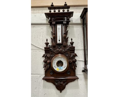 A late 19th century wall hanging aneroid barometer with thermometer, with extensive Black Forest style carved decoration and 
