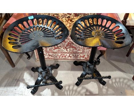 A pair of tractor seat rise and fall bar stools with four splay feet and twisted foot rest.