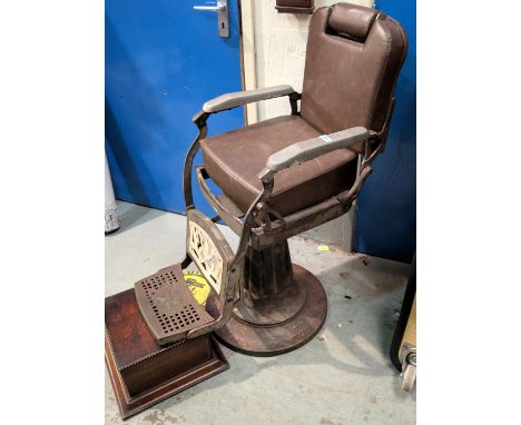 A vintage metal barber's chair with arm rests, foot rest, large base.
