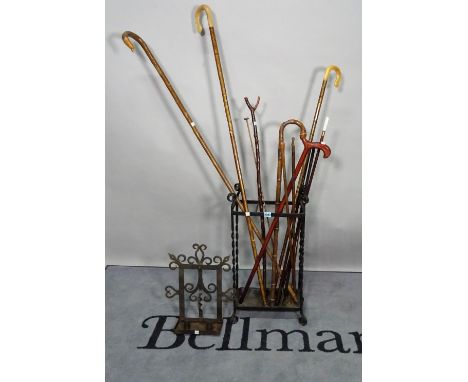 Six various canes in a wrought-iron stick stand, 38cm wide x 76cm high, and a wrought-iron twin-light candle stand, 36cm wide