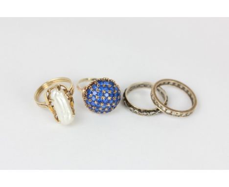 A domed cluster ring set with round blue stones in yellow gold, a white stone eternity ring, a white stone full hoop eternity