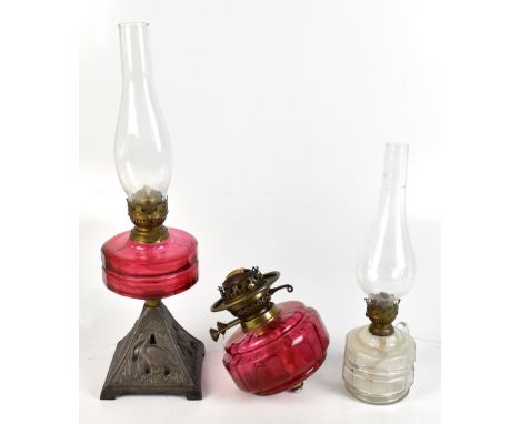 A late 19th century oil lamp with cranberry glass reservoir raised on cast iron stand decorated with cranes, height including