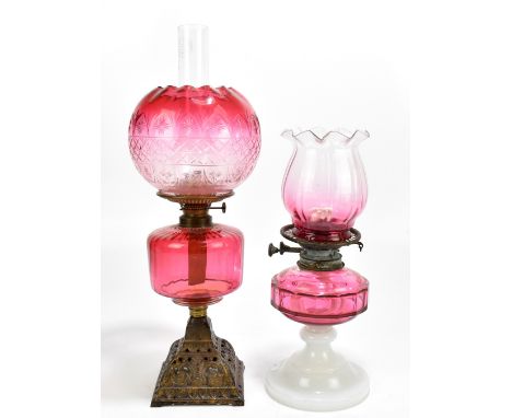 A late Victorian oil lamp with cut cranberry shade and reservoir, raised on pierced metal plinth base, overall height includi